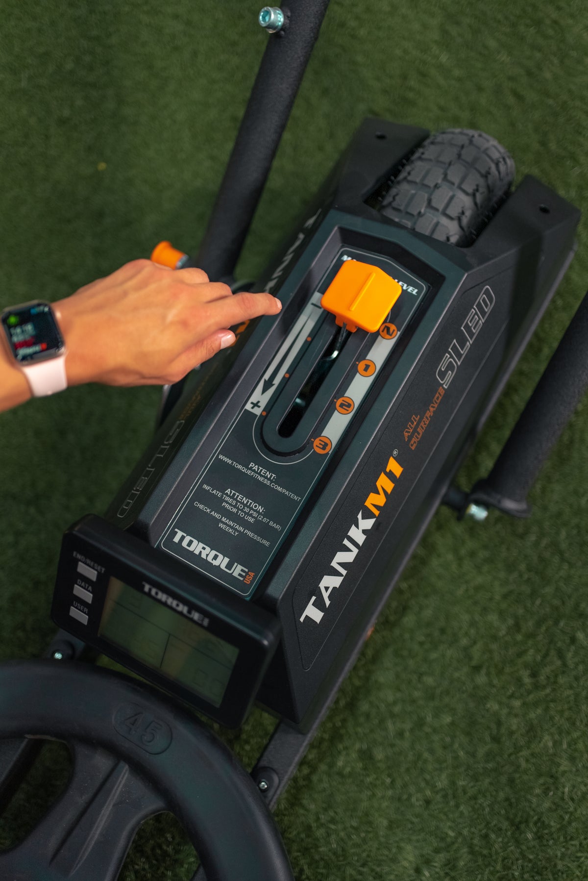 Person adjusting the resistance level of a TANK M1 push sled.