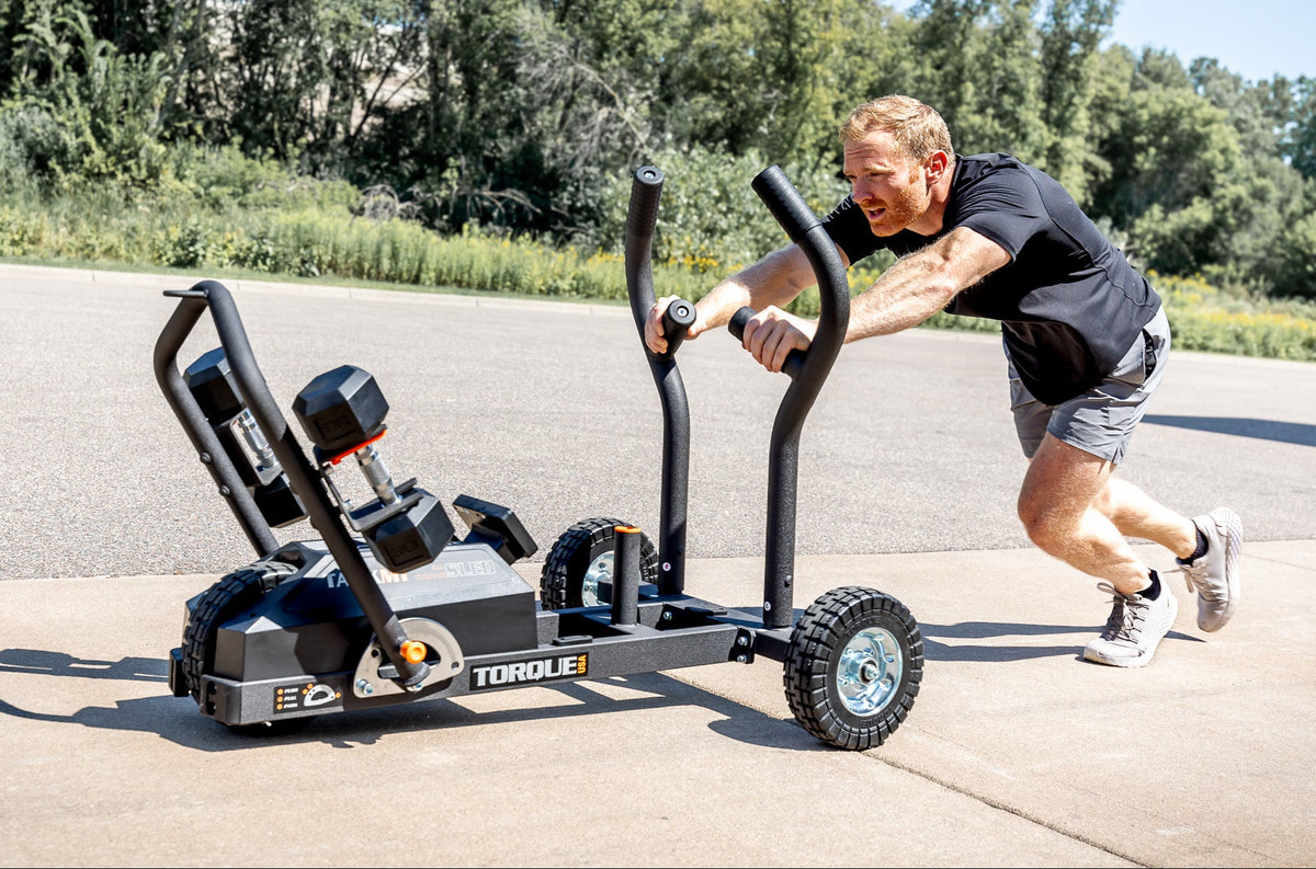 A man pushing a TANK M1 resistance sled in a concrete parking lot.