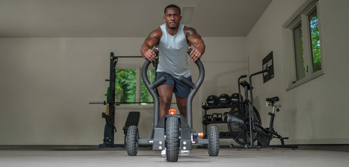 A man is pushing a TANK M1 resistance sled in his garage gym.