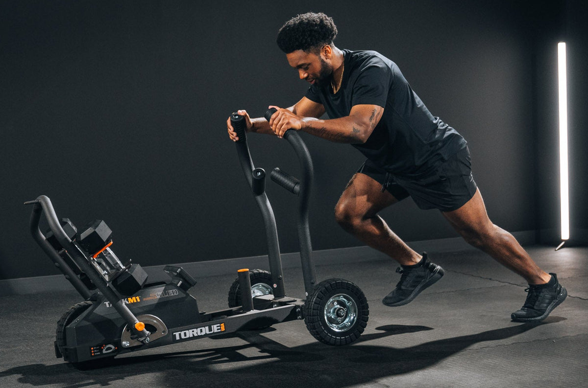 Man pushing a TANK M1 in a gym space
