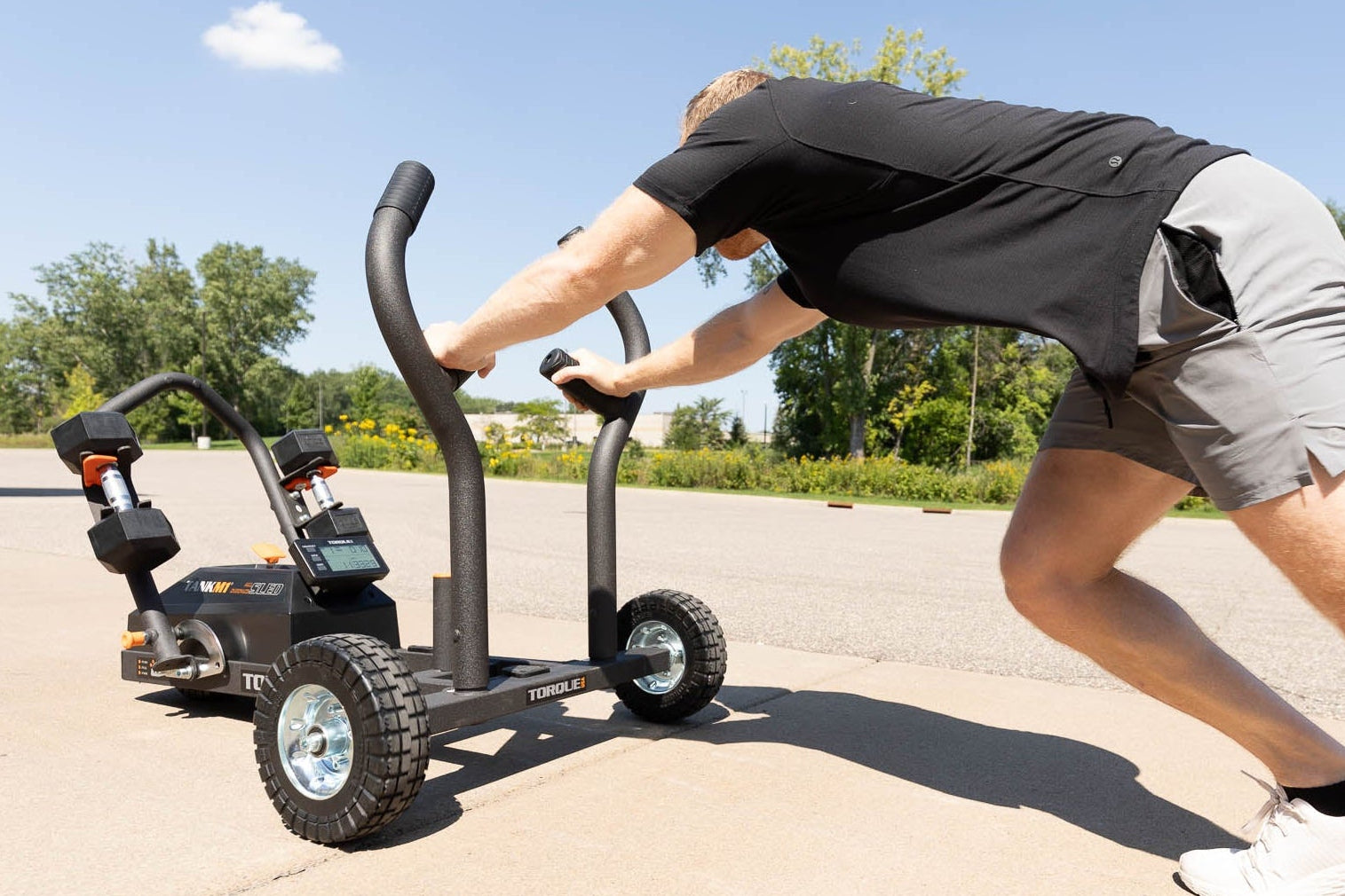 A man pushing a TANK M1 Resistance Sled on a concrete parking lot.
